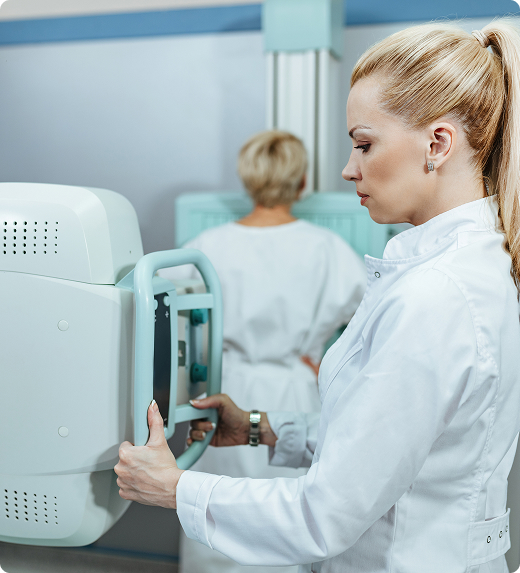 Un médico sostiene y controla una máquina de rayos X mientras un paciente se encuentra en el fondo siendo escaneado