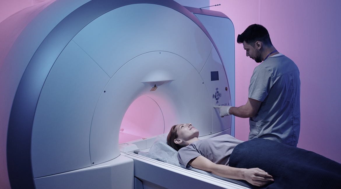 Un técnico presiona botones en una máquina de resonancia magnética mientras un paciente espera una resonancia magnética